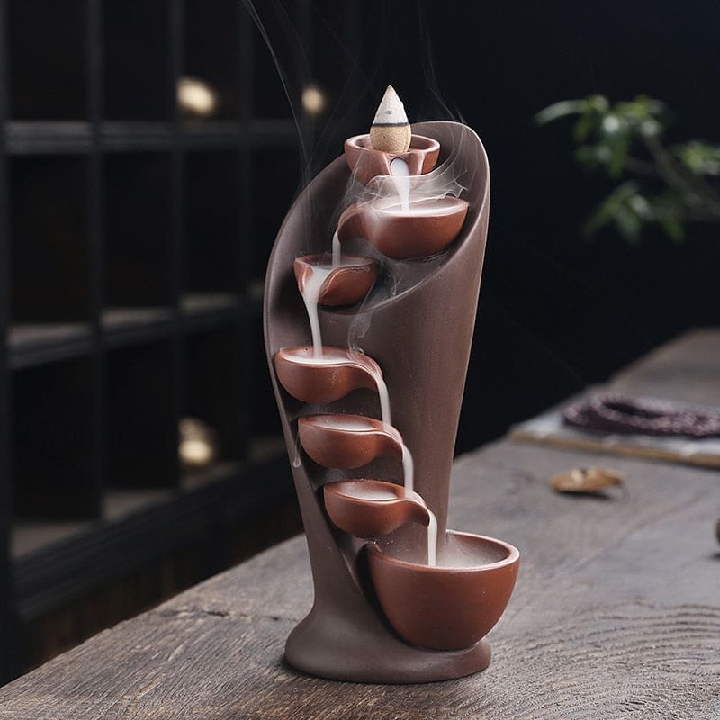 Full front view of the brown incense burner, with smoke spilling between its small curved bowls into the larger base basin.