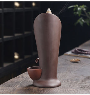 Rear view of the brown backflow incense burner, showing its smooth curved back and the side of the lowest bowl.