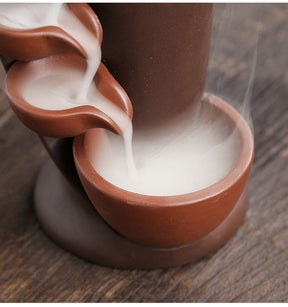Detailed view of white incense smoke pooling in the bottom brown bowl beneath the descending channel.