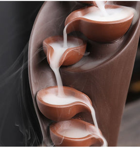 Close-up of the brown waterfall burner's upper tiers, with smoke spilling from one rounded bowl into the next.