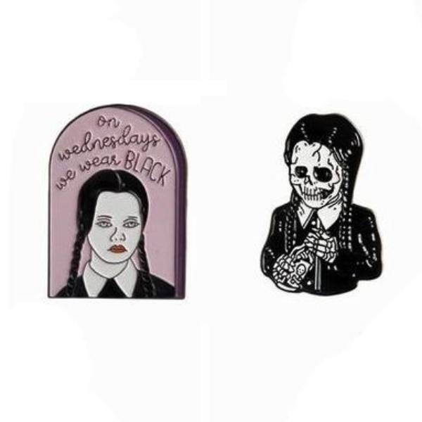 Two braided portrait enamel pins on white: a pink arched We Wear Black design and a black-and-white skeleton figure.
