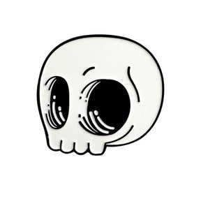 White cartoon skull enamel pin isolated on white, with oversized black eye sockets, curved highlights and a rounded outline.