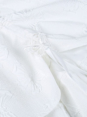Detail of a white butterfly accent beside a ribbon loop on the gathered skirt, with raised butterfly motifs visible across the fabric.