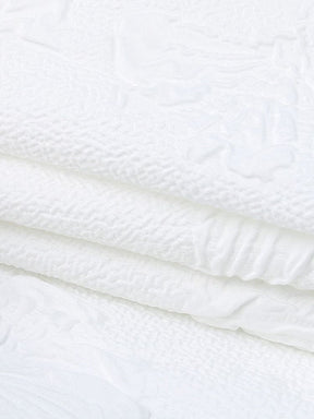 Detail view of the white dress fabric and finished edge, with raised butterfly motifs and small leaves across the surface.