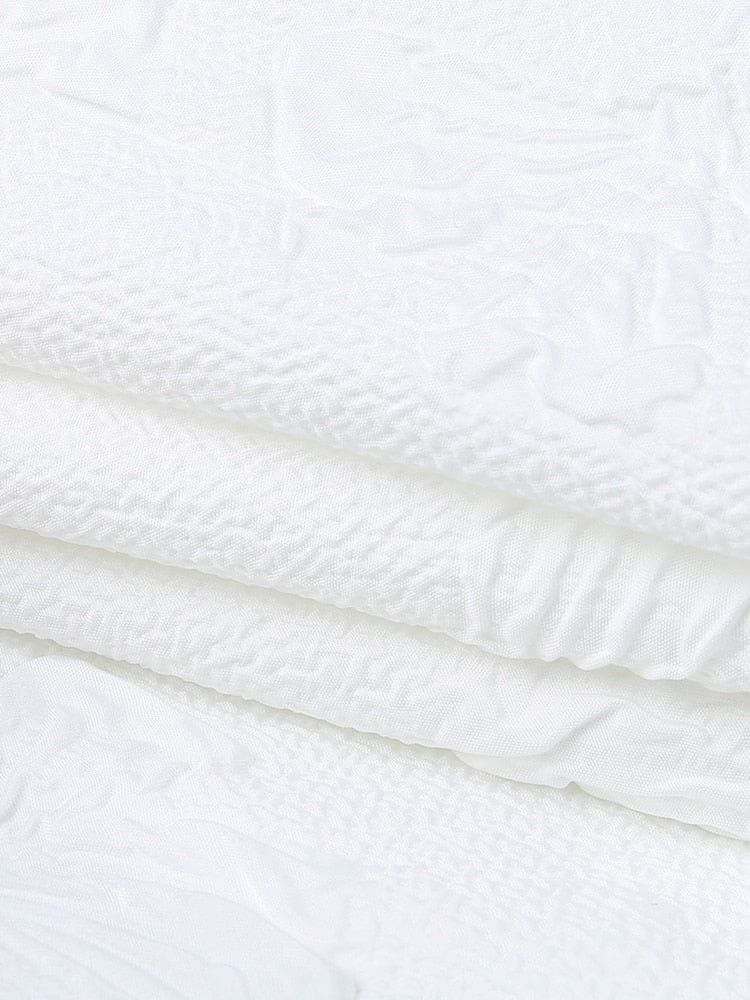 Detail view of the white dress fabric and finished edge, with raised butterfly motifs and small leaves across the surface.