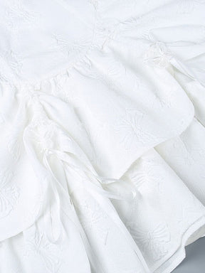 Close-up of butterfly-textured white skirt panels gathered with ribbon ties and small butterfly accents. The layered fabric and trailing ribbons fill the image.