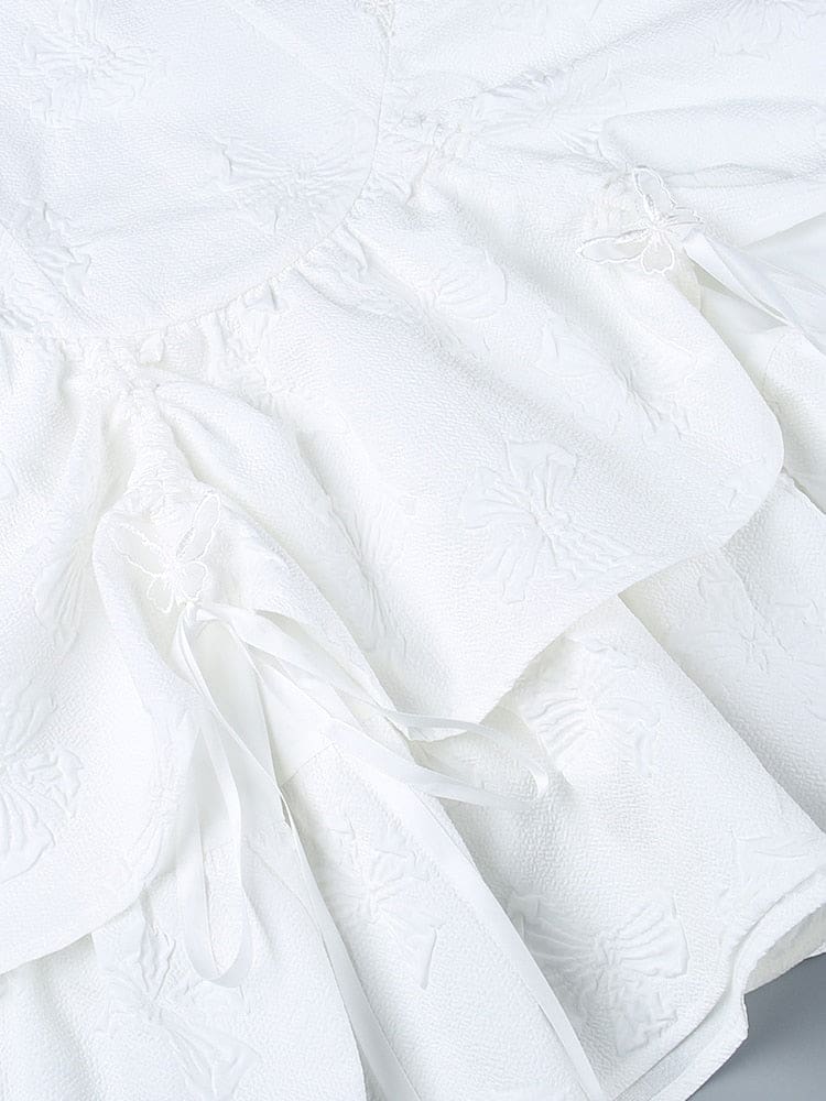 Close-up of butterfly-textured white skirt panels gathered with ribbon ties and small butterfly accents. The layered fabric and trailing ribbons fill the image.