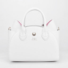 White cat-ear handbag shown cleanly from the front against white, with pink inner ears, twin handles and a gold-tone crescent centred above small lettering.