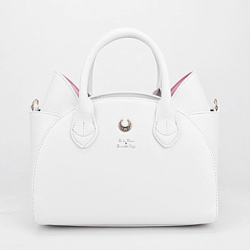 White cat-ear handbag shown cleanly from the front against white, with pink inner ears, twin handles and a gold-tone crescent centred above small lettering.
