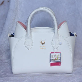 White cat-ear handbag with pink ear panels, a gold-tone crescent and matching handles, photographed with protective wrapping and retail tags.