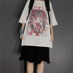Fuller outfit view of the white anime graphic T-shirt with a black backpack, frayed black shorts and a patterned wrist covering, photographed against a gray wall.
