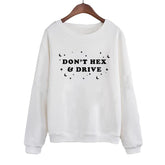 White crewneck sweatshirt on a wooden hanger, with black DON’T HEX & DRIVE lettering surrounded by crescent moons, stars and dots. Long sleeves end in ribbed cuffs above a matching ribbed hem.