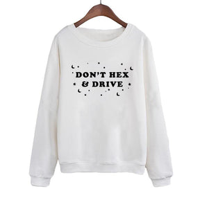 White crewneck sweatshirt on a wooden hanger, with black DON’T HEX & DRIVE lettering surrounded by crescent moons, stars and dots. Long sleeves end in ribbed cuffs above a matching ribbed hem.