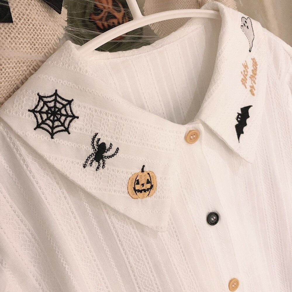 Close-up of the white blouse on a hanger, showing a spiderweb, spider and orange pumpkin embroidered on one pointed collar tip.