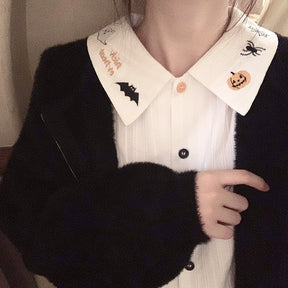 White Halloween blouse worn under a black cardigan, with its embroidered pointed collar and orange-and-black button line exposed.