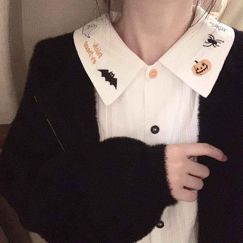 White Halloween blouse worn under a black cardigan, with its embroidered pointed collar and orange-and-black button line exposed.