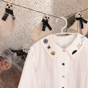 White Halloween blouse hanging beneath small skull-and-bow decorations, with its embroidered pointed collar and alternating buttons visible.