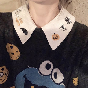 White Halloween collar worn over a dark cartoon graphic sweater, with black bat, spider and pumpkin embroidery framing the neckline.