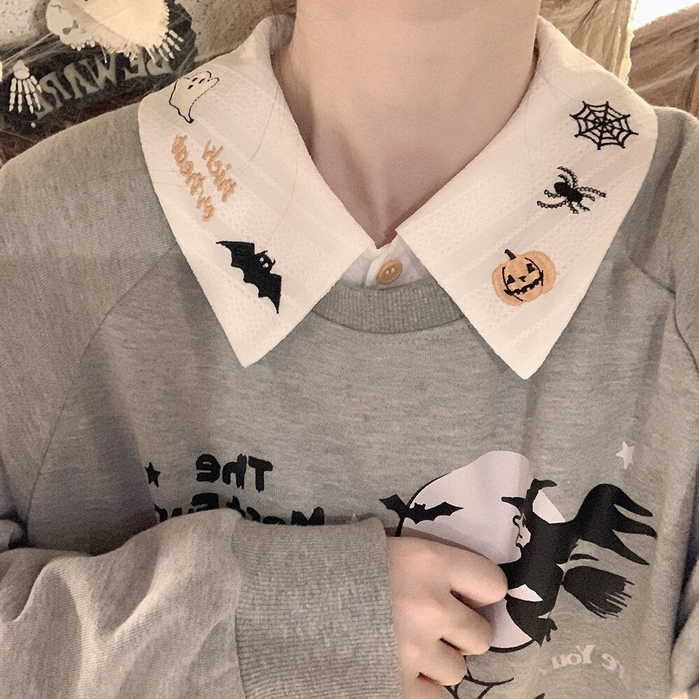 Close view of the white embroidered Halloween collar over a gray witch-print sweatshirt, showing the pumpkin and spiderweb on one point.