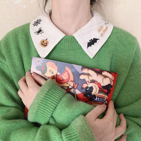 White Halloween blouse collar layered above a green knit cardigan, with a printed card held below the black bat embroidery.