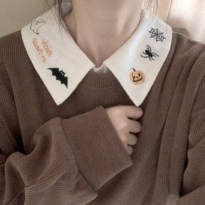 White Halloween blouse collar worn above a brown knit top, with pumpkin, spider and bat embroidery visible around the neck.