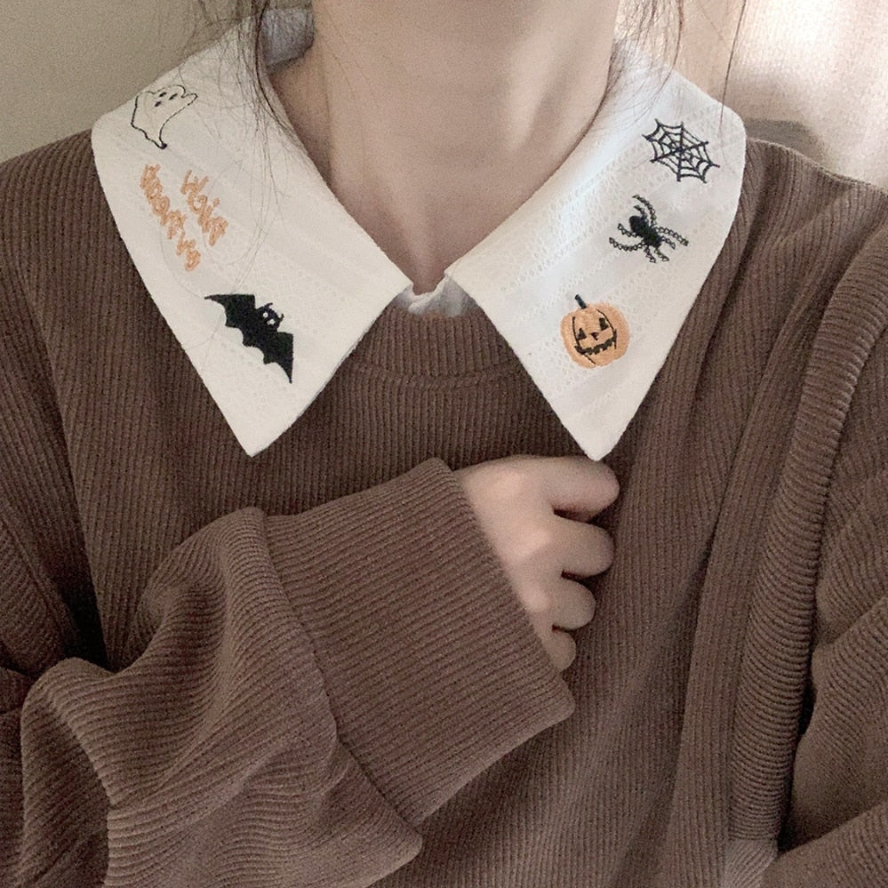 White Halloween blouse collar worn above a brown knit top, with pumpkin, spider and bat embroidery visible around the neck.