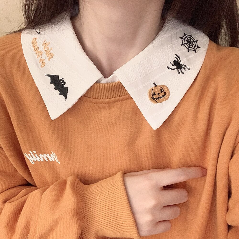 White pointed Halloween collar layered over an orange sweatshirt, highlighting the black spiderweb and orange pumpkin stitching.