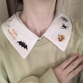 White Halloween collar worn with a pale green sweatshirt, showing embroidered ghost, bat and pumpkin motifs against the light layers.