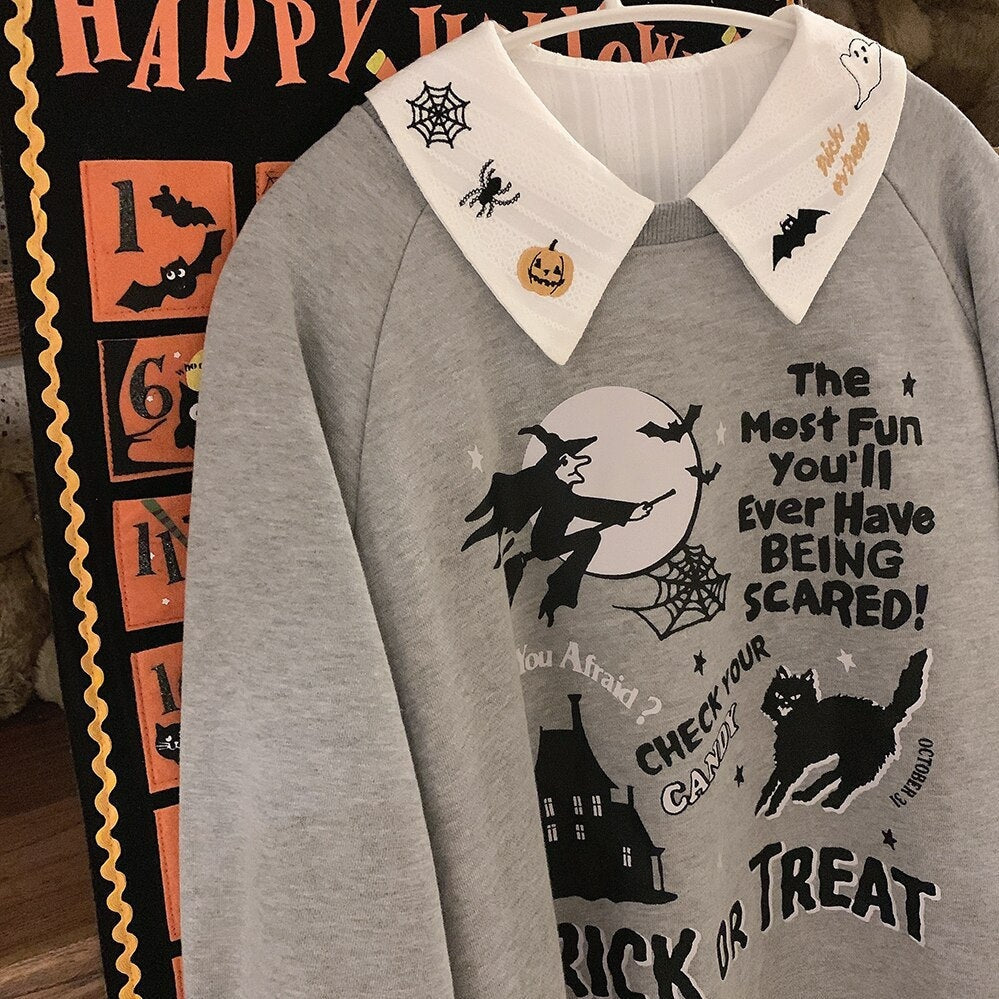 White embroidered Halloween blouse layered under a gray Trick or Treat sweatshirt on a hanger beside an orange Halloween wall graphic.