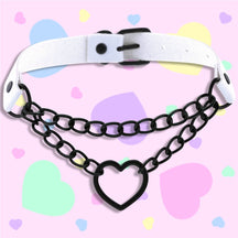 White faux leather choker with two black chain rows and an open heart centerpiece, displayed against a pink background scattered with pastel hearts.