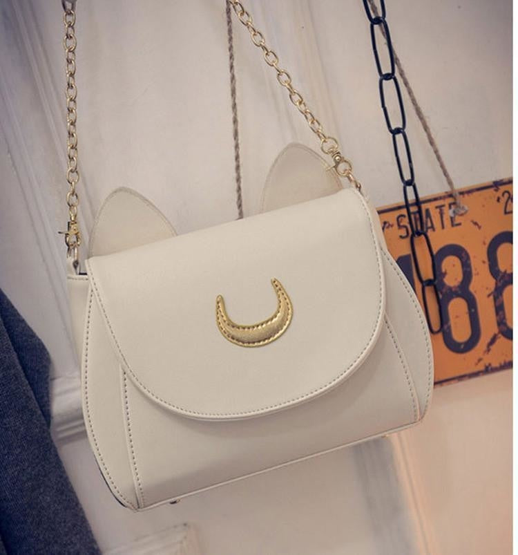 White cat-ear moon bag hanging from its gold-tone chain, with the curved flap and crescent emblem shown from the front.