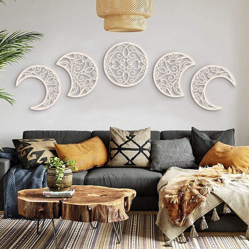 White scrollwork moon-phase wall art above a dark sofa, with the open cutouts allowing the pale wall to show through.