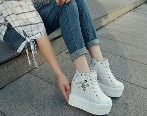 White high-top platform sneakers worn with cuffed jeans on gray steps, showing the metal eyelets and skull zipper pulls.