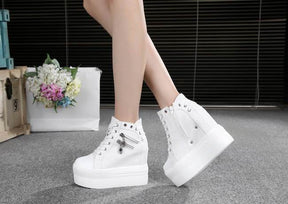 White platform wedge sneakers worn with crossed ankles, showing skull pulls and the raised heel profile.