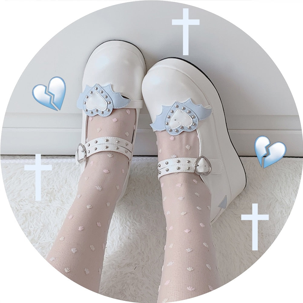 White winged-heart platform Mary Janes worn with sheer white stockings, showing blue heart-and-wing accents beneath decorative cross graphics.