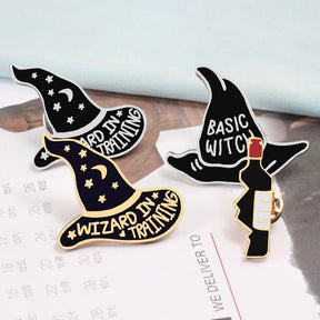 Black and purple pointed-hat enamel pins arranged beside a small decorative bottle, showing different lettering and metallic outlines.