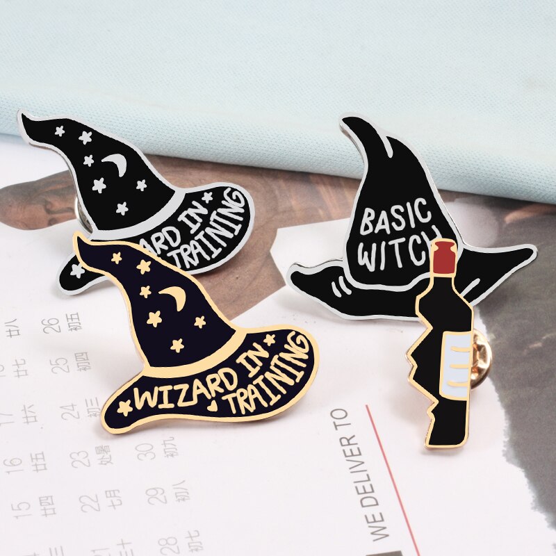 Black and purple pointed-hat enamel pins arranged beside a small decorative bottle, showing different lettering and metallic outlines.