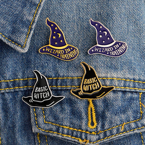 Four black and purple hat pins attached to denim, showing the Basic Witch and Wizard in Training sayings together.