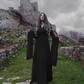 Black velvet gown worn beside stone ruins under a gray sky, with both sleeves hanging in deep points.
