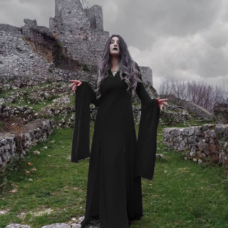 Black velvet gown worn beside stone ruins under a gray sky, with both sleeves hanging in deep points.