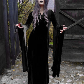 Full-length black gown beside an open wooden gate, with arms extended to display the draped sleeves.