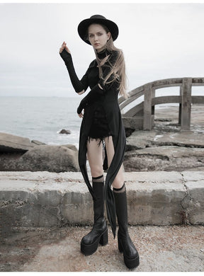 Black asymmetric layering dress worn with a raised hand, highlighting the extended sleeve cuffs and split pointed hem against a seaside background.