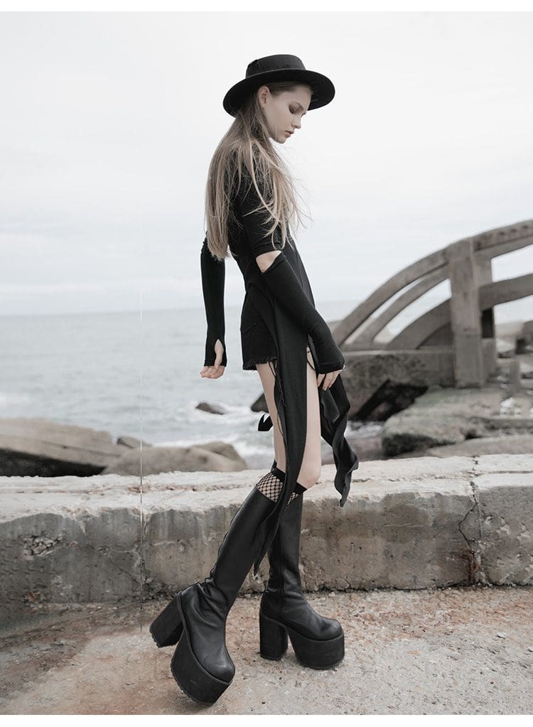 Rear three-quarter view of a black witchy layering dress beside the sea, showing the fitted back, sleeve opening and pointed lower panels.