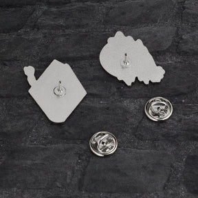 Reverse sides of the spellbook and crystal ball pins, each with a single post. Their removable silver-tone butterfly-clutch backs lie beside them on dark fabric.
