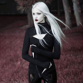 Black gothic turtleneck shown outdoors with the collar folded down and arms crossed, emphasizing the diagonal zip and angular hem.
