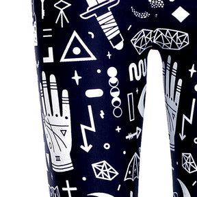 Close view of the white occult-inspired print on black leggings, showing a marked palmistry hand, dagger, pointed crystals and moon phases.