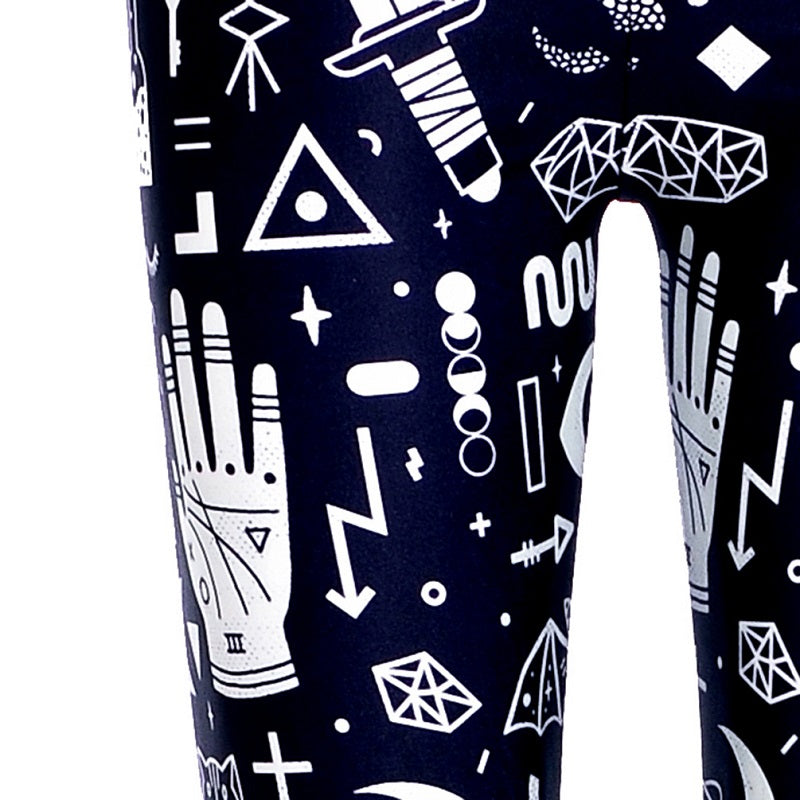 Close view of the white occult-inspired print on black leggings, showing a marked palmistry hand, dagger, pointed crystals and moon phases.