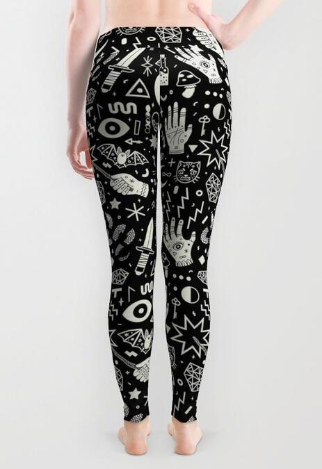 Black occult-print leggings worn by a barefoot model viewed from behind, with white illustrations continuing across the hips and legs against grey.