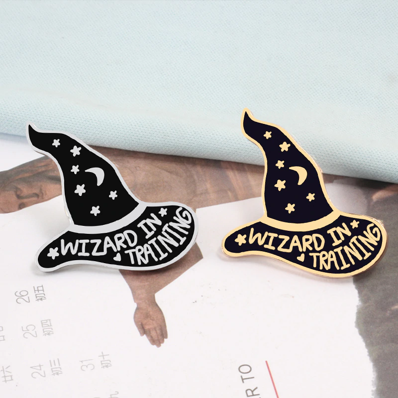 Purple Wizard in Training hat pins arranged together on printed paper, showing both metallic finishes.