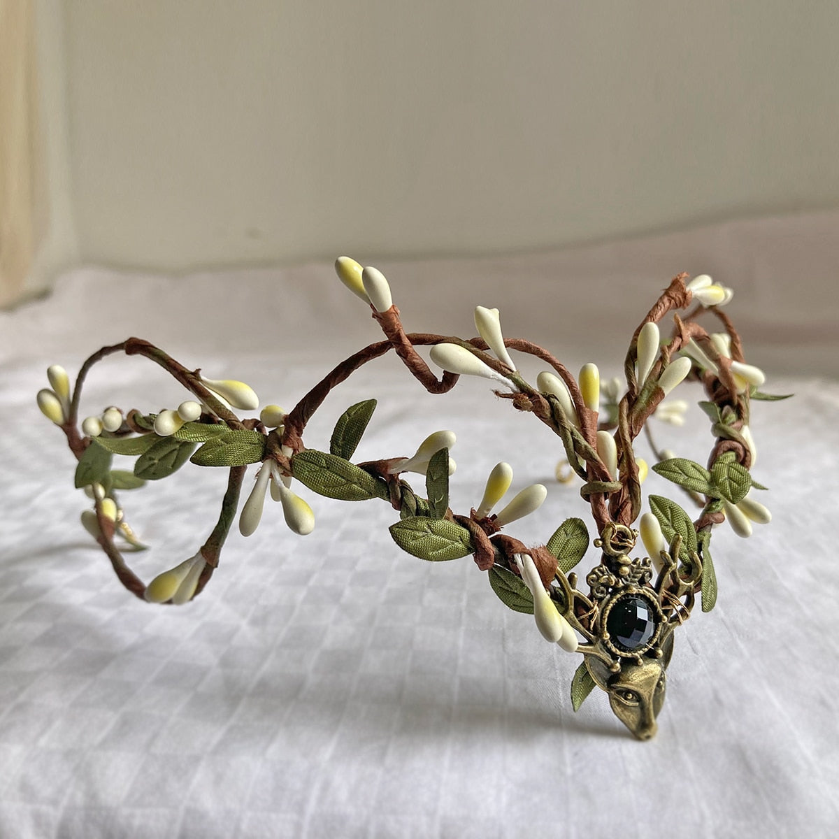 Brown vine-style tiara with pale buds, green leaves and a dark round accent above a deer-head centrepiece.